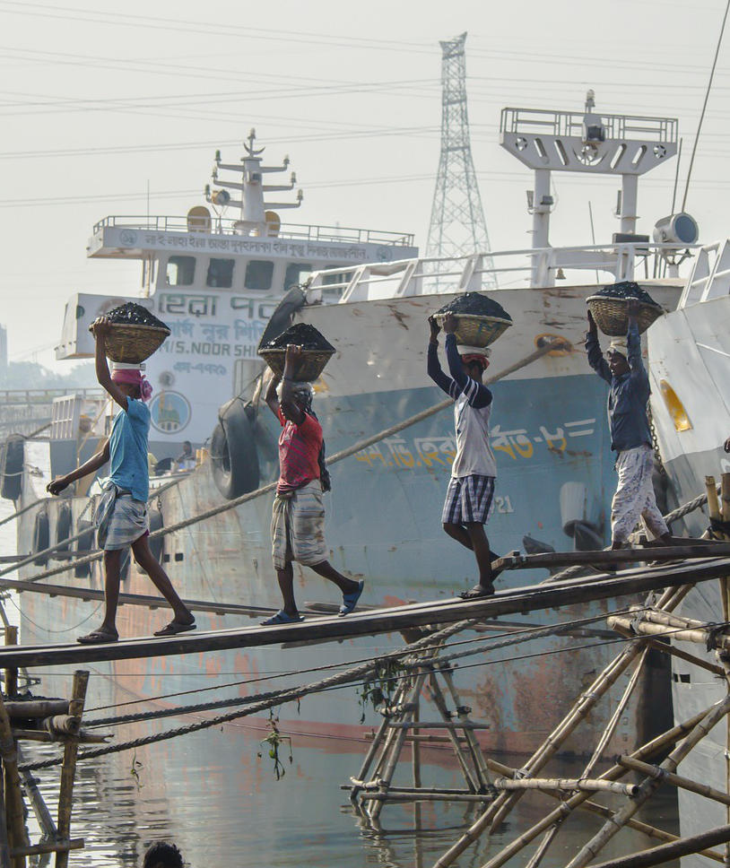 four men with baskets on their heads walking across a gang plank from a ship