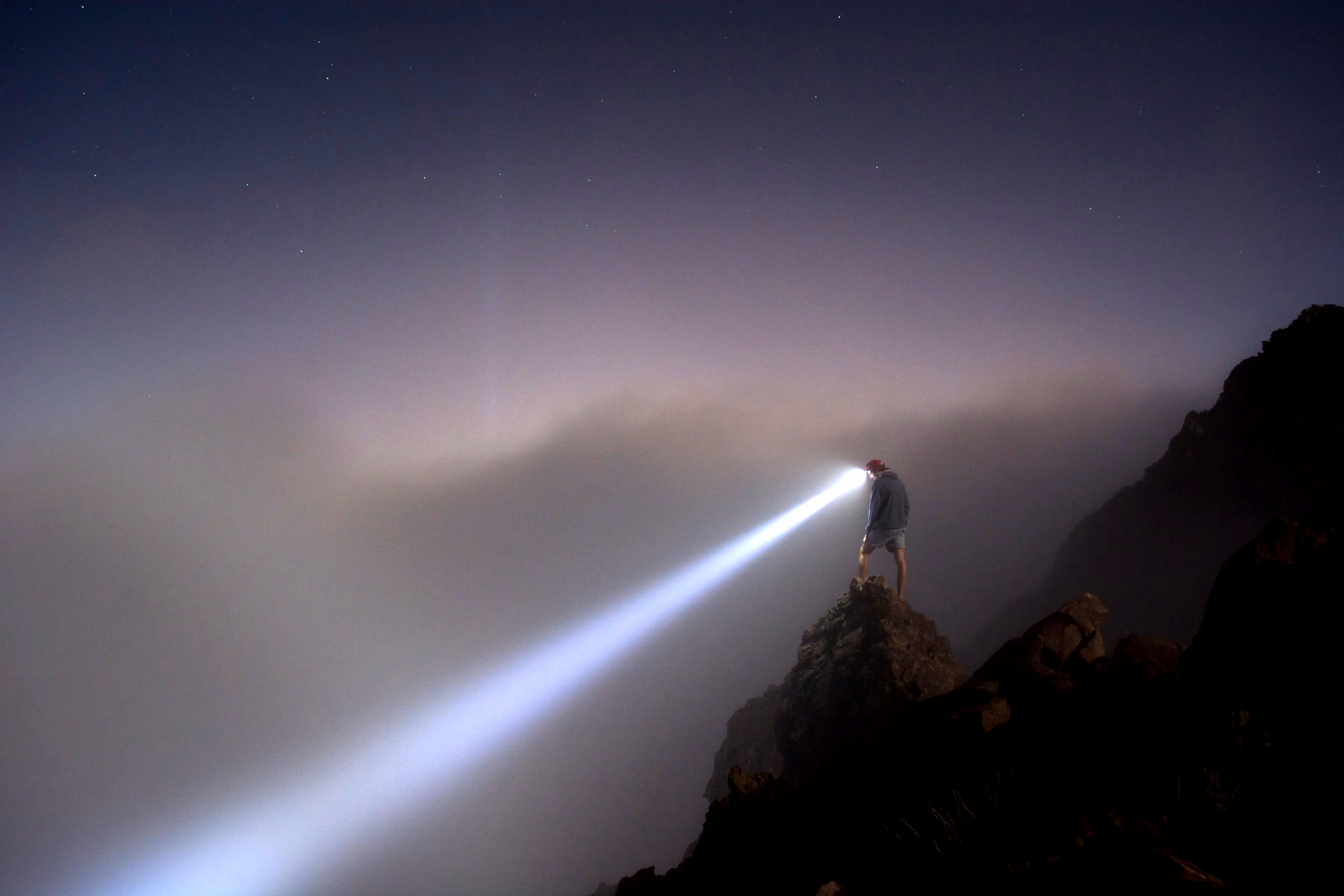 person with a bright head lamp standing on a rock shining headlamp down